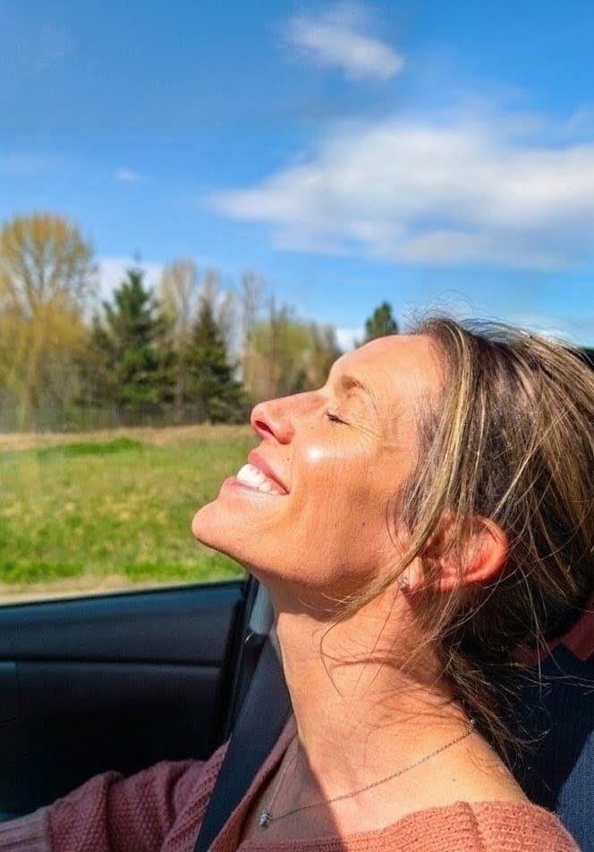 Awbria in a convertible, face turned toward the sun